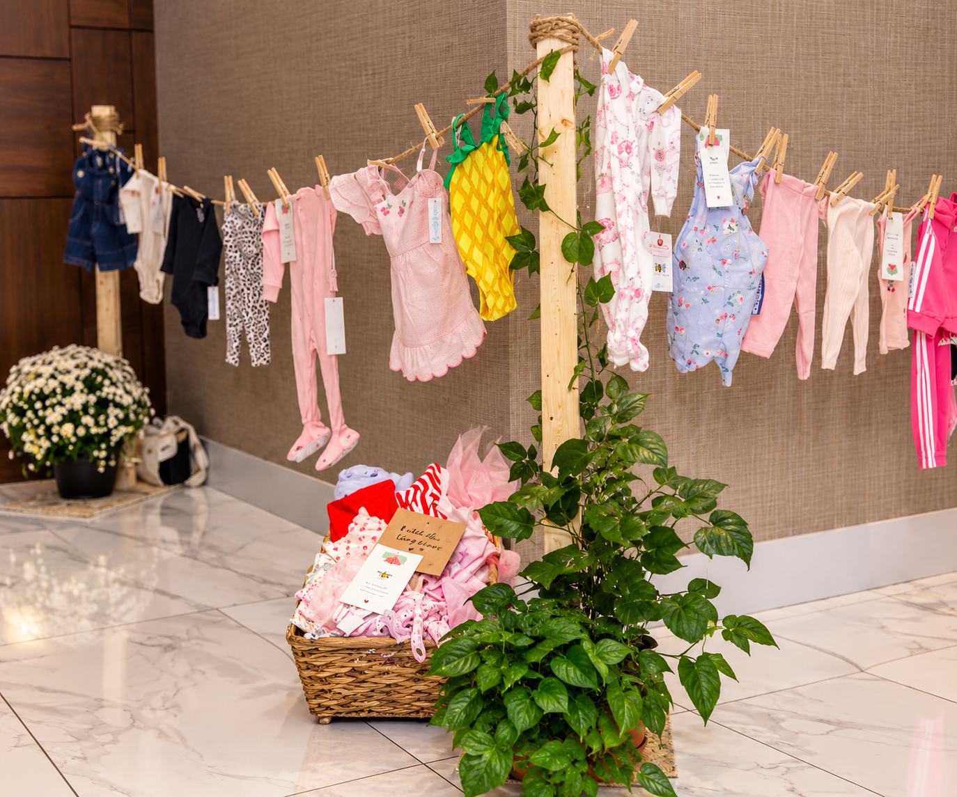 Baby shower display with a clothesline of baby outfits and greenery