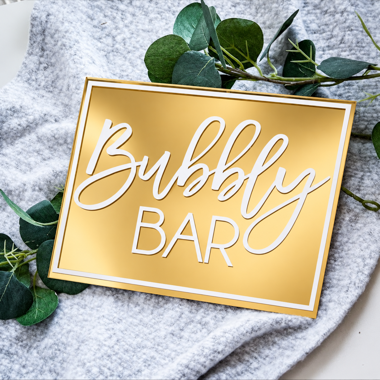Gold Bubbly Bar sign with white lettering and greenery